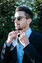 Fashionable man adjusting his suit and sunglasses outdoors on a sunny day.